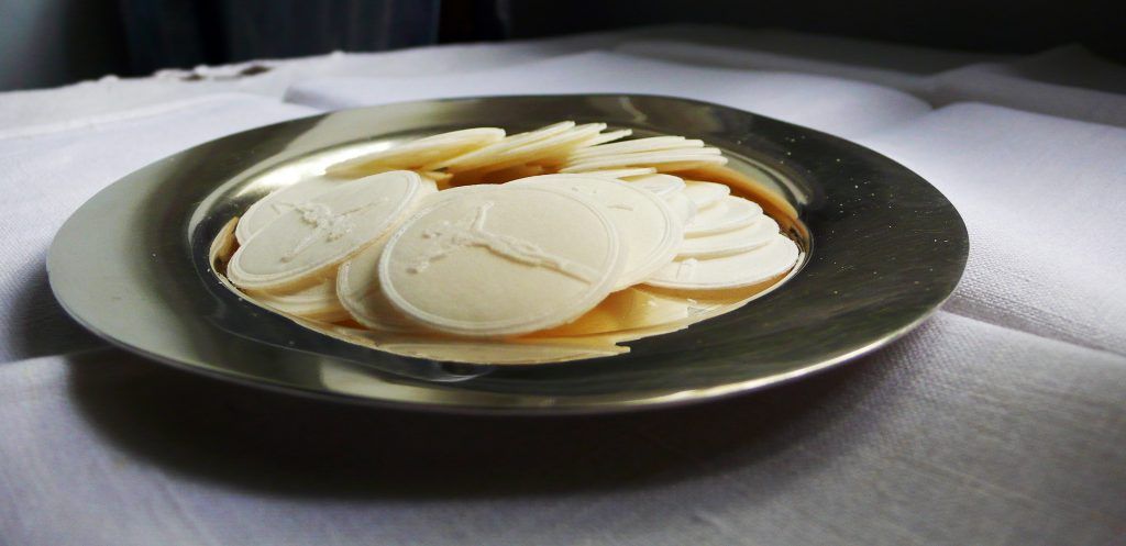 A silver plate holds many white communion wafers on a white tablecloth.