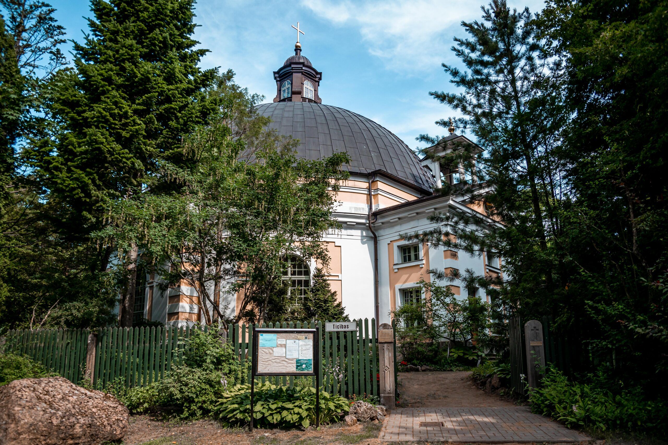 A historic white building with a dark dome roof surrounded by dense green trees.