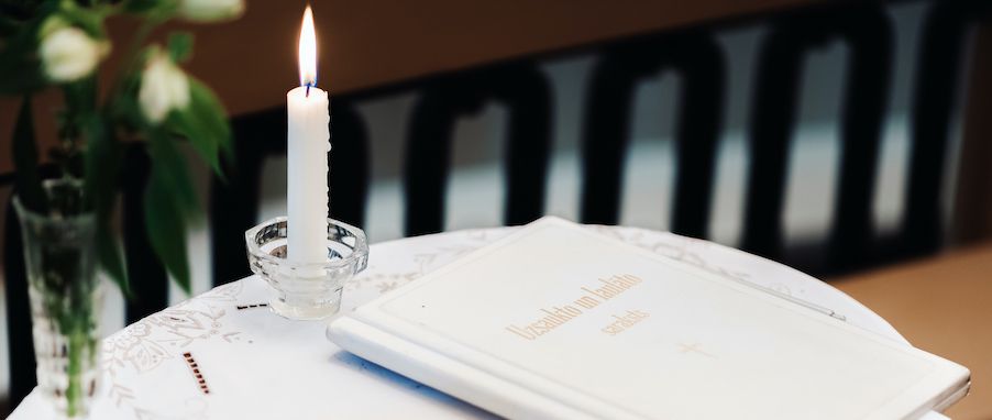 A flickering white candle and a decorative white book rest on a lace tablecloth.